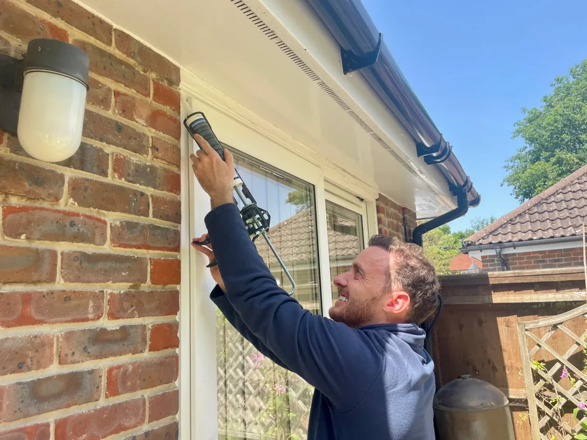Mr Mastic applicator sealing the top of a white uPVC door frame on a red-brick house