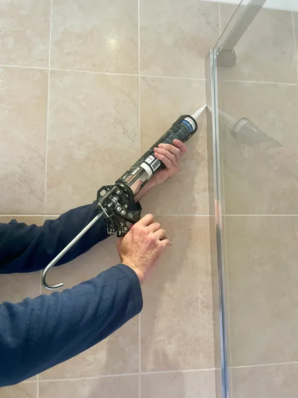 Fresh white silicone going into the corner where a shower screen meets the tiled wall